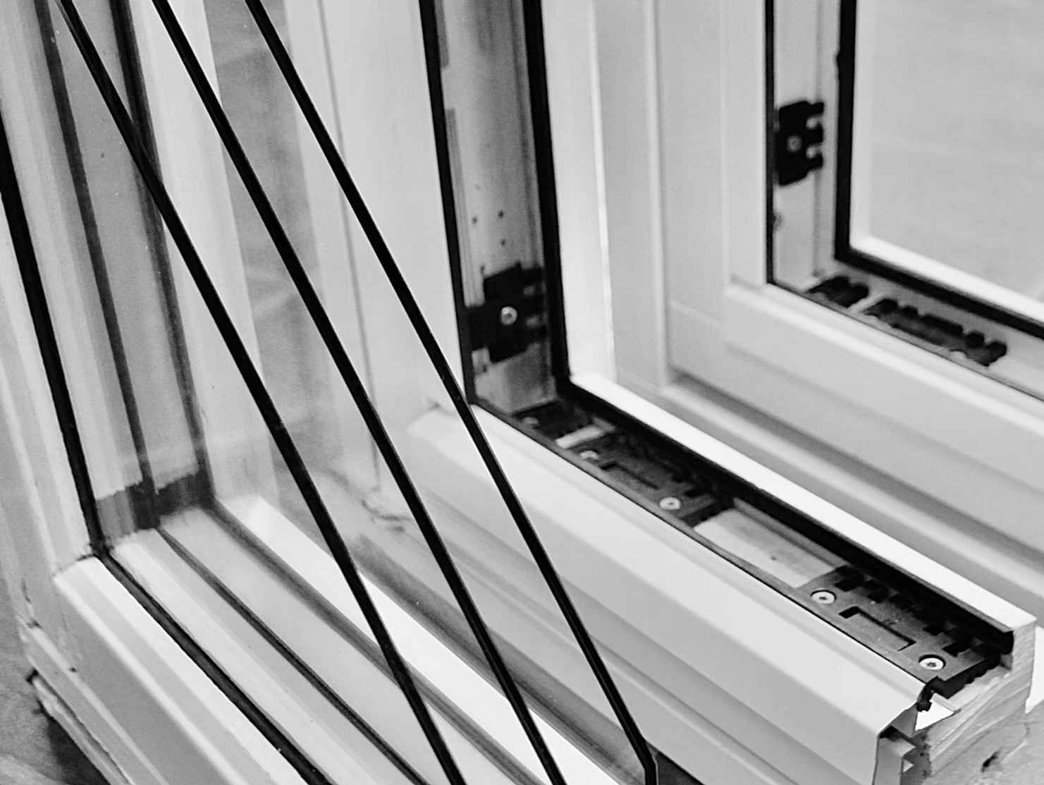 Nærbilde i sort-hvitt av et vindushjørne med flere glasslag og detaljer i rammen.